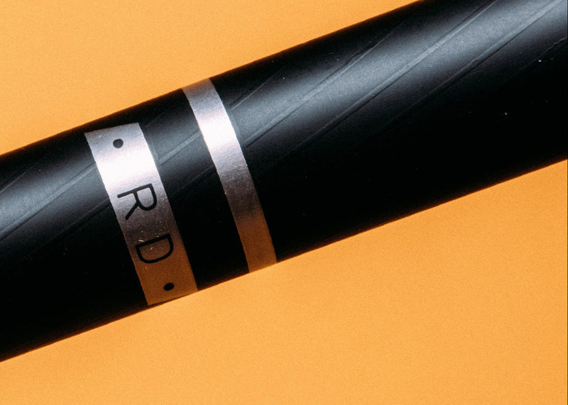 Close-up of a black floorball shaft with 'RD' branding on an orange background