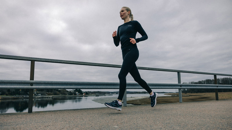 Person running on a road with a cloudy sky and water in the background